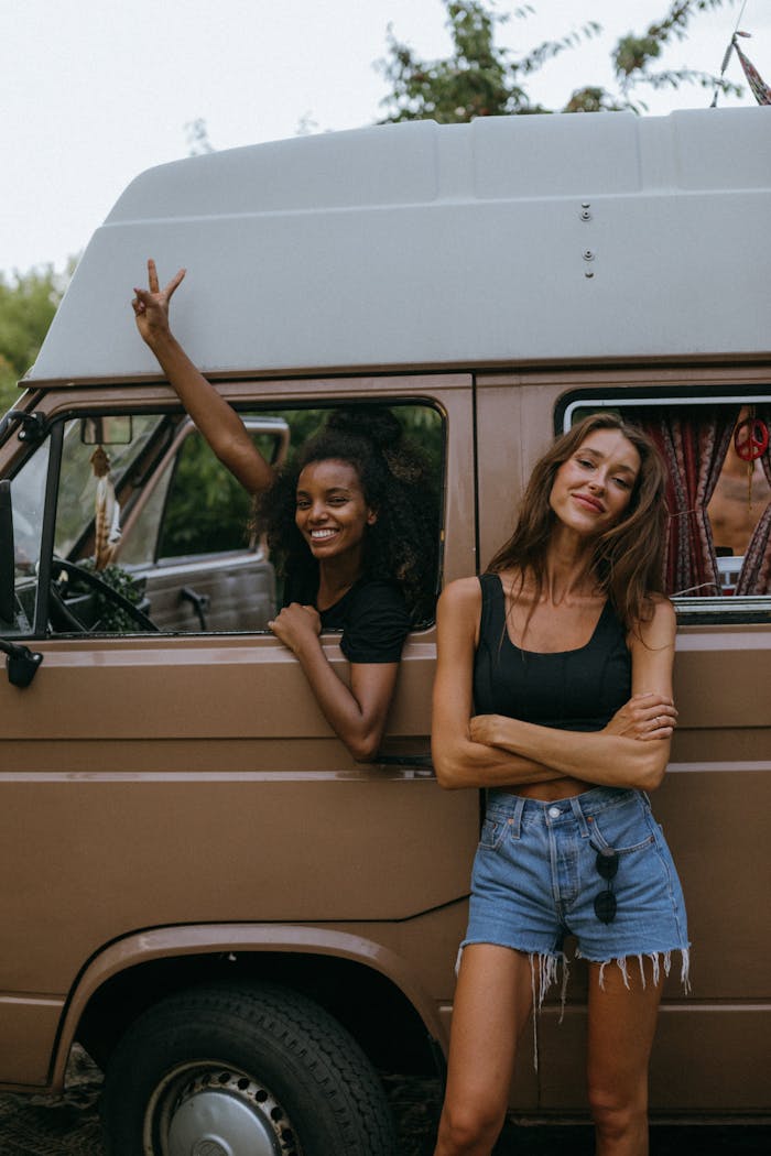 Two women enjoying a fun road trip, posing beside a vintage camper van outdoors.